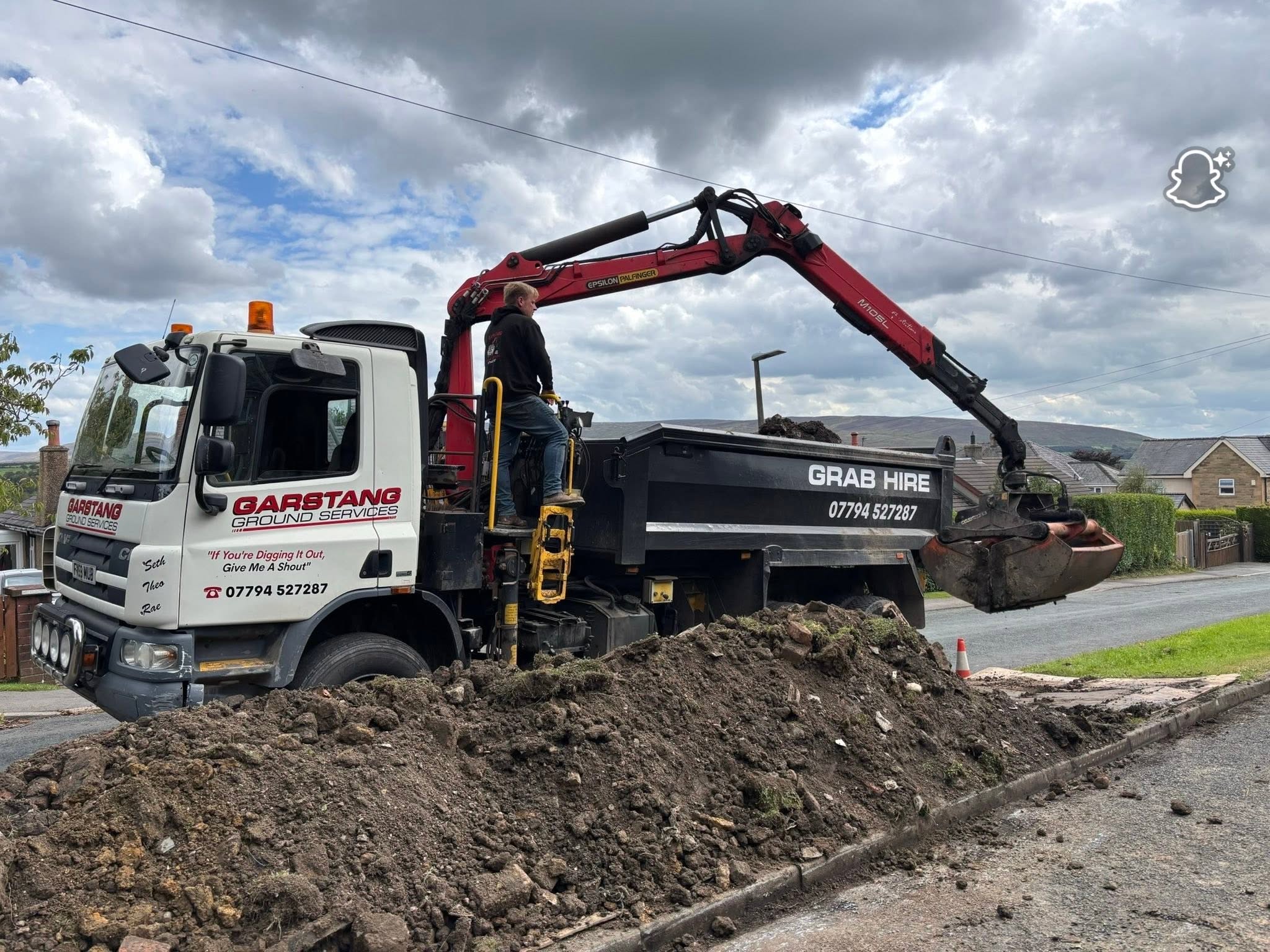 Man operating a grab lorry to clear soil off the side of the road